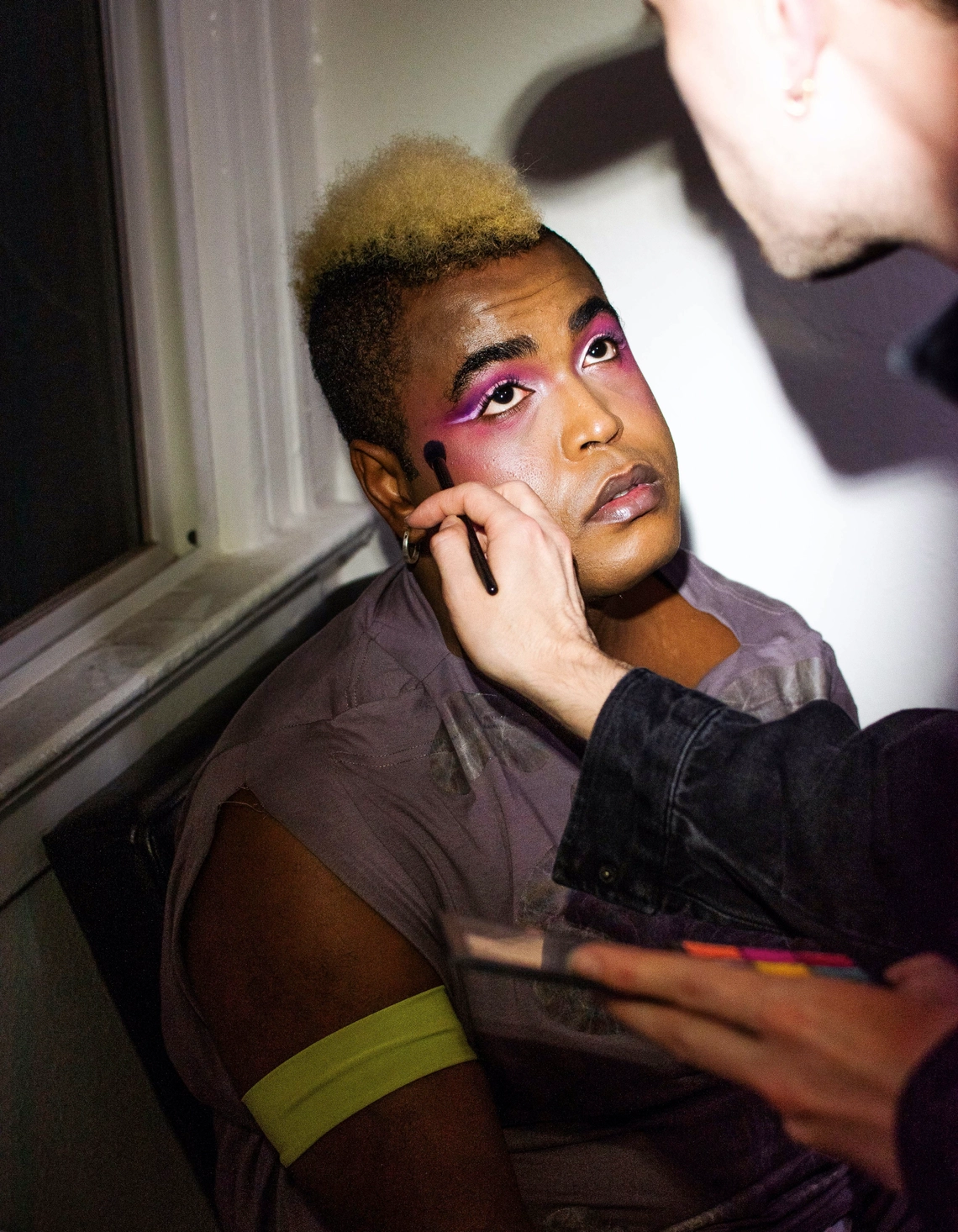 DJ Miss Parker getting their makeup done by Jesse Clark, looking up at Jesse while eyeshadow is applied